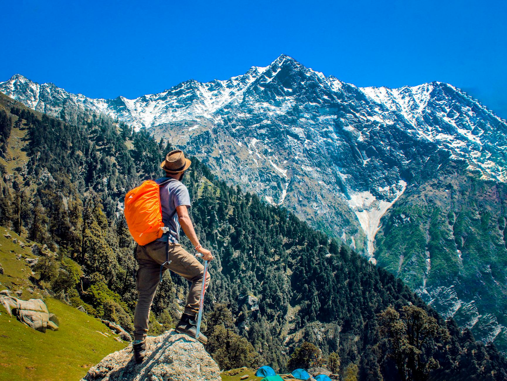 man wearing blue shirt standing on cliff while watching mountain